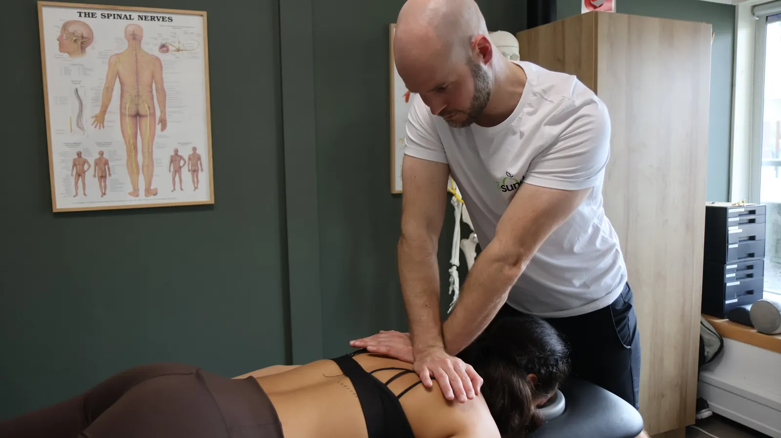 David Brink behandler brystryggen på en patient, der ligger på maven på briksen.