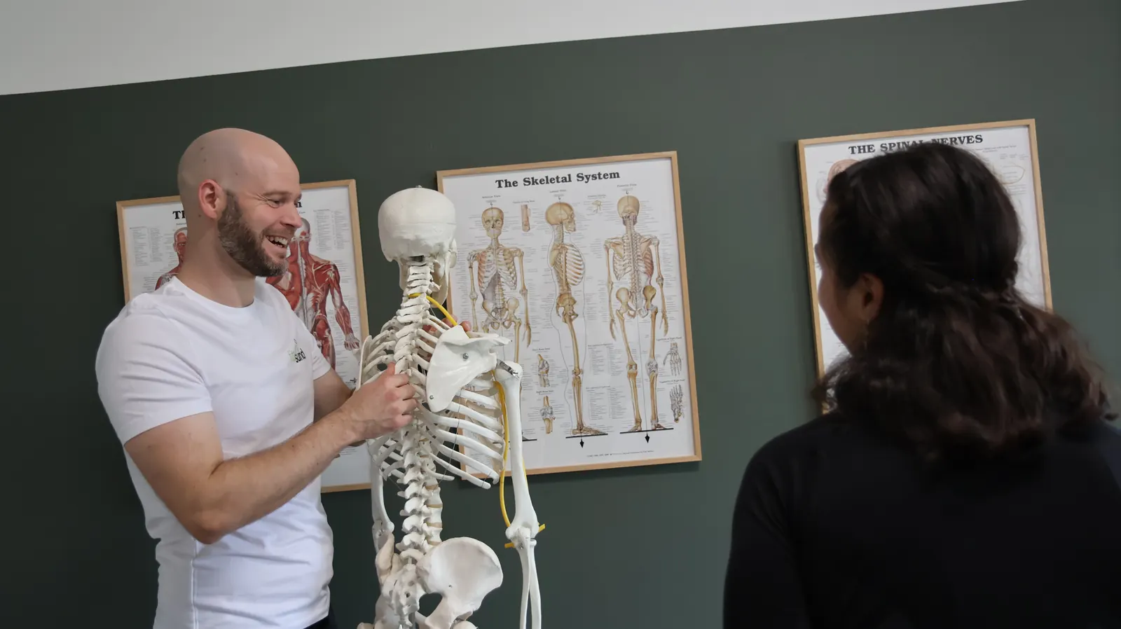 David Brink smiler og viser på et skelet, hvordan skulder og ryg hænger sammen.